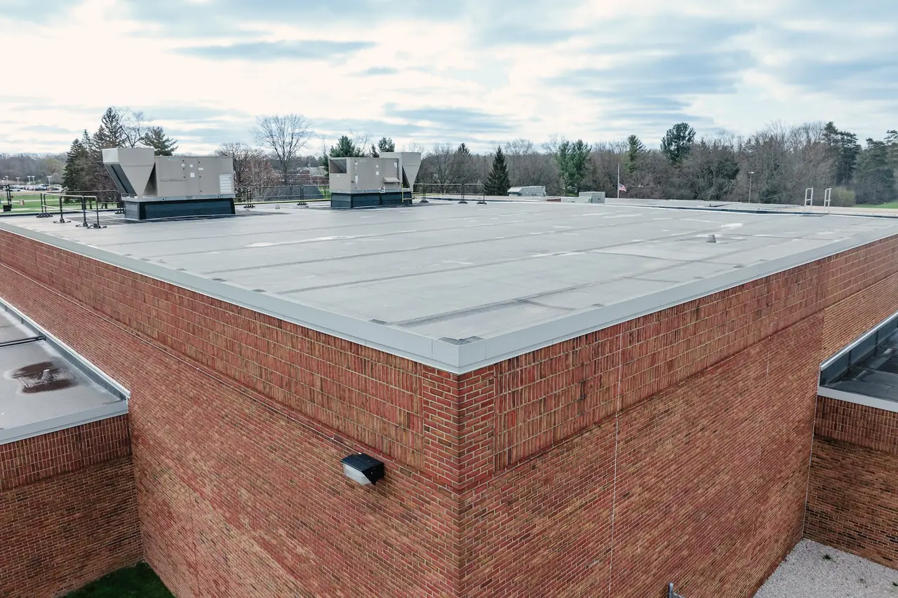 Low-slope membrane roof at Solon Elementary meeting a brick wall capped with metal coping